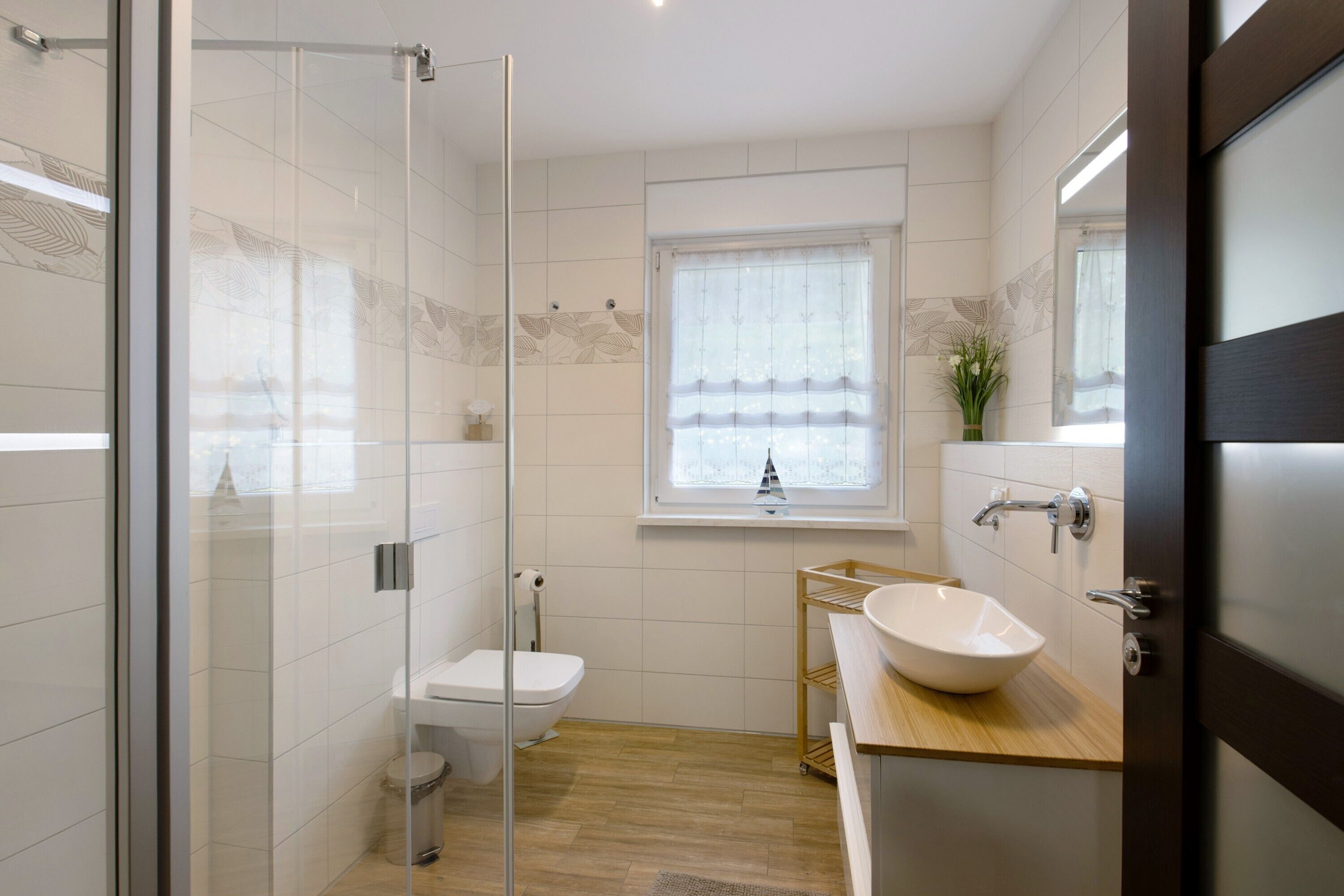 Un baño moderno con cabina de ducha de vidrio, inodoro, lavabo y ventana con cortina.