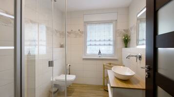 Un baño moderno con cabina de ducha de vidrio, inodoro, lavabo y ventana con cortina.