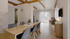 Uma área de refeições com uma mesa de madeira, cadeiras cinzas, uma TV montada na parede e uma planta sobre um armário.