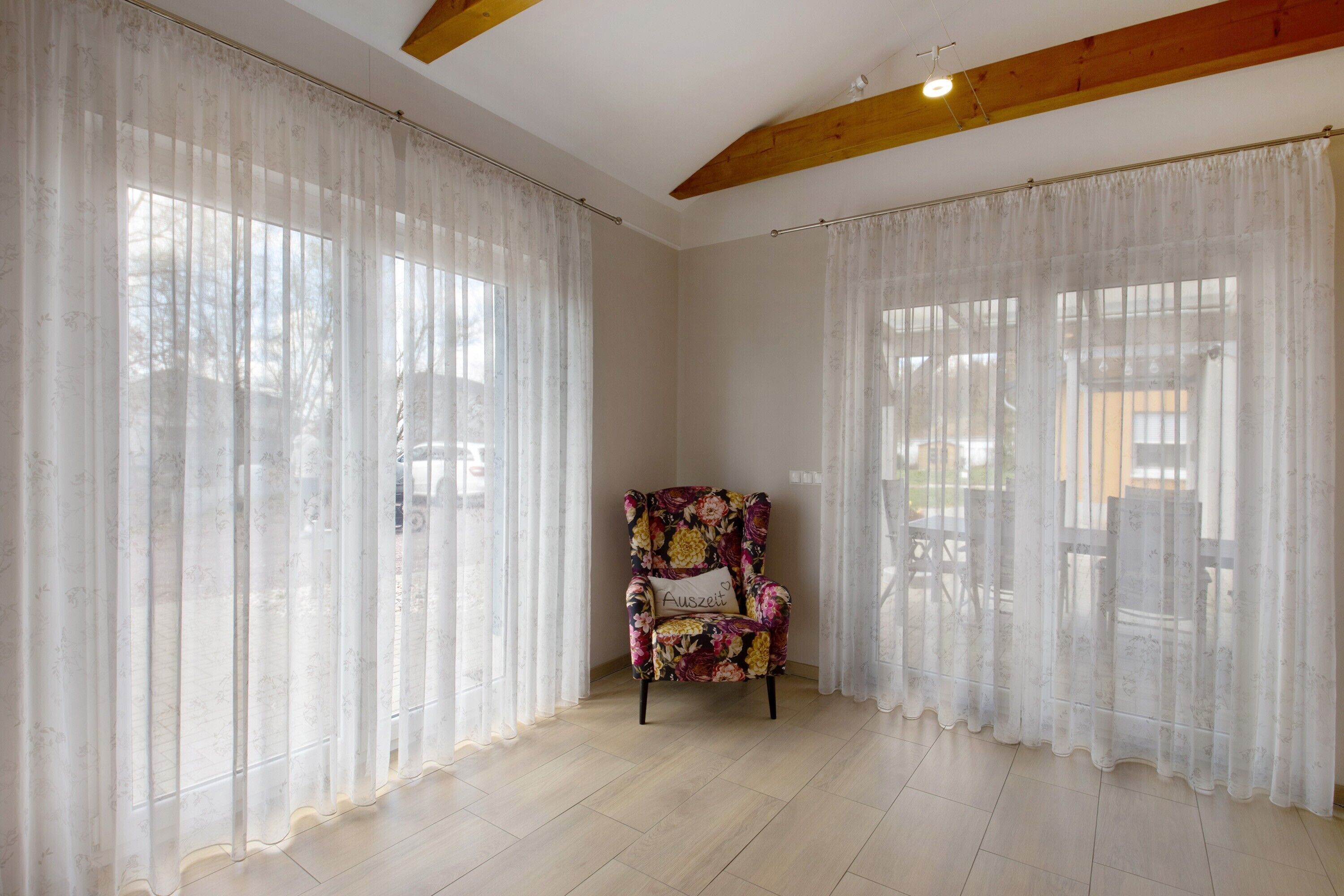Ein Zimmer mit großen Fenstern, einem floralen Sessel und einem Holzbalken an der Decke.