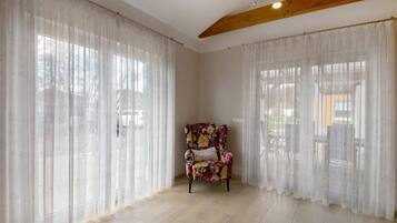Ein Zimmer mit großen Fenstern, einem floralen Sessel und einem Holzbalken an der Decke.