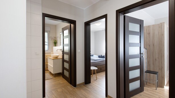 Um interior moderno com piso de madeira, um banheiro com pia e espelho, e um quarto com cama e poltrona.