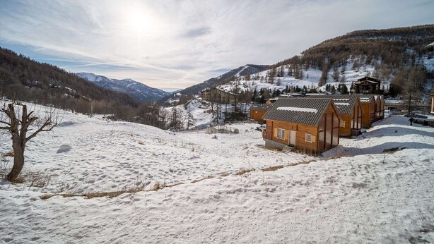 Un paisaje nevado con una cabaña de madera y una montaña al fondo.