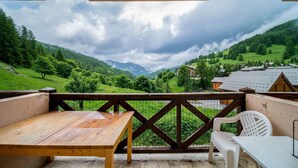 Un balcón con mesa y sillas de madera, con vistas a un valle verde con casas y montañas.
