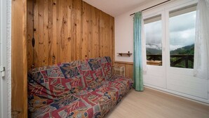 Una habitación con paneles de madera, un sofá de colores vivos, una puerta blanca que da a un balcón y una pequeña mesa.