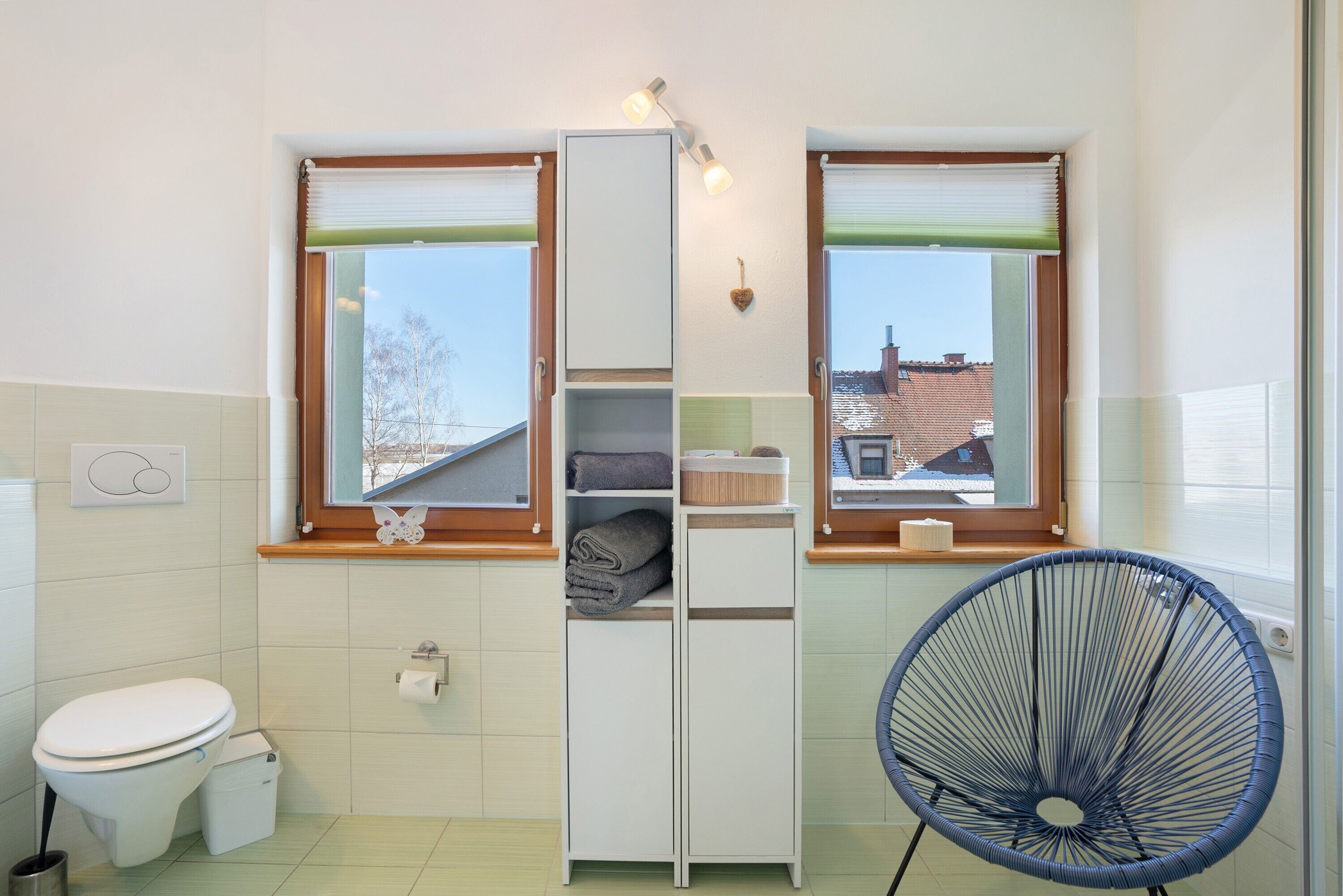 Een badkamer met toilet, wastafel, handdoekrek en een raam met uitzicht op gebouwen.