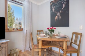 Et spiseområde med et træbord, stole, en vase med blomster og et billede på væggen.