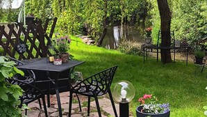 A garden patio with a table and chairs, surrounded by greenery and a pond. - Apartment 'Spreequartier' with Lake View, private Terrace and Wi-Fi (Malschwitz)