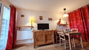 Ein gemütliches Wohnzimmer mit Fernseher, Holzschrank, Esstisch und Stühlen.