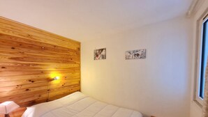 Ein Schlafzimmer mit einem Holz-Kopfteil, einem Bett mit weißer Decke, zwei Wandlampen und zwei kleinen Bildern.
