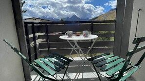 Ein Balkon mit Tisch und Stühlen, Blick auf die Berge und einen klaren Himmel.