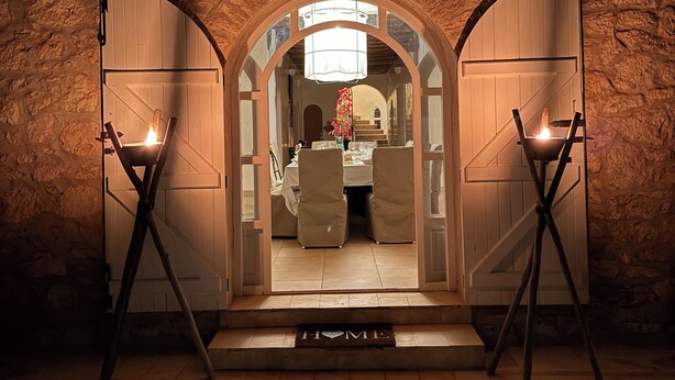 An arched doorway leading into a room with a table set for dining, a candle on each side, and a 'HOME' mat at the entrance. - A haven of peace in the countryside surrounded by 90 olive and 10 argan trees (Essaouira)