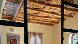 A cozy living room with a large window, a wooden ceiling, and a painting on the wall. - A haven of peace in the countryside surrounded by 90 olive and 10 argan trees (Essaouira)