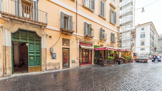A cobblestone street with a building featuring a green door and a red awning. - View of Campo de Fiori (Roma)