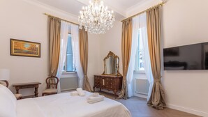 A hotel room with a large bed, a dresser, a mirror, a chandelier, and a flat-screen TV. - View of Campo de Fiori (Roma)