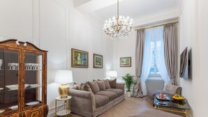 A living room with a brown sofa, a glass cabinet, a chandelier, and framed pictures on the wall. - View of Campo de Fiori (Roma)