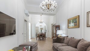 A spacious living room with a large chandelier, a brown sofa, and a dining area with a table and chairs. - View of Campo de Fiori (Roma)