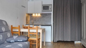 Un espacio habitable compacto con kitchenette, zona de comedor con mesa y sillas, y sofá con cojines estampados.