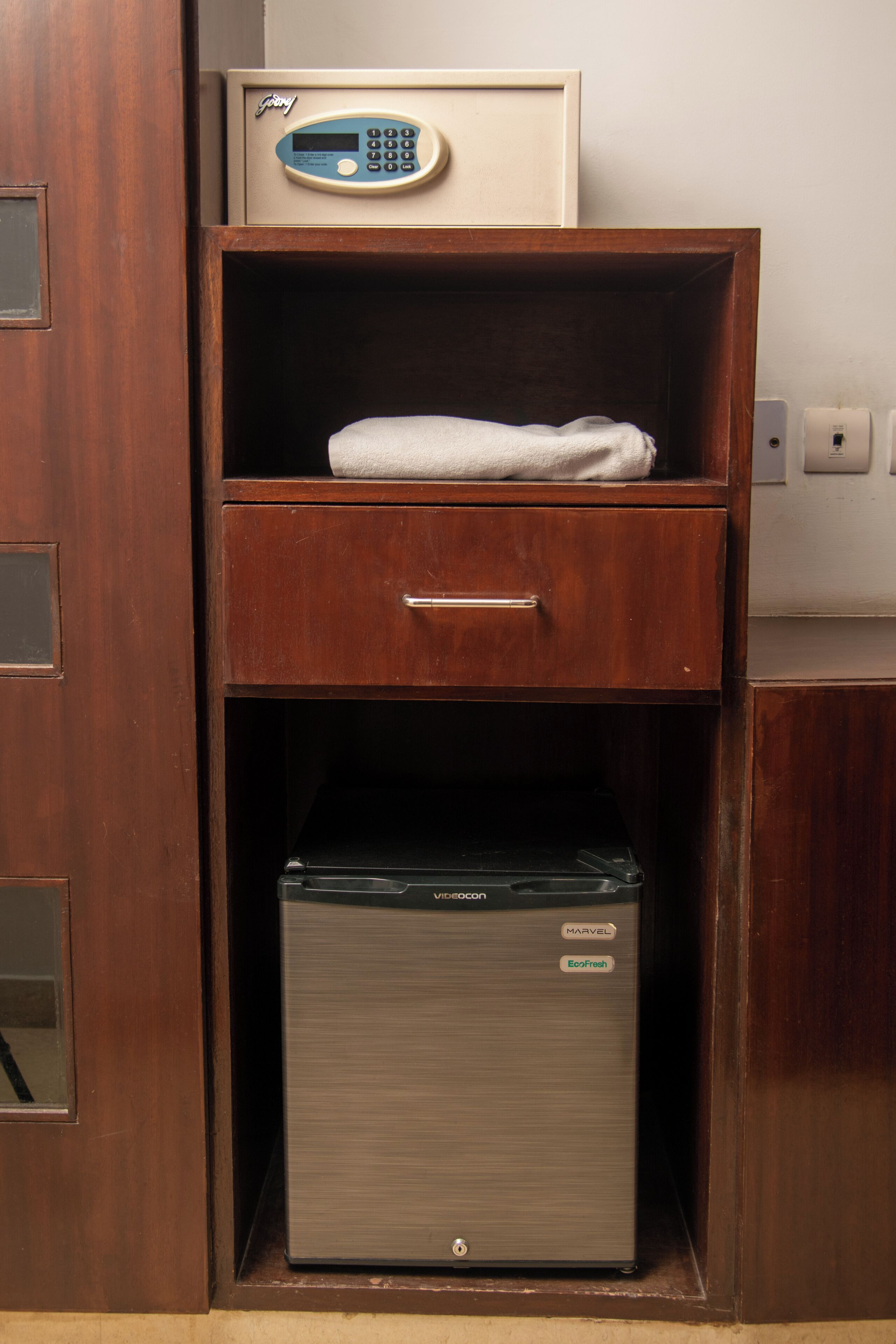 Een houten kast met een magnetron bovenop, een lade eronder en een kleine koelkast onderin.