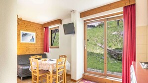 A cozy room with a wooden dining table, chairs, a sofa, a TV mounted on the wall, and a sliding glass door leading to a garden. - Stay with Garden, Chamrousse (Chamrousse)