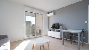 Ein modernes Wohnzimmer mit einem weißen Sofa, einem runden Tisch und einem Essbereich mit Tisch und Metallstühlen.
