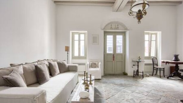 A room with a white sofa, a wooden coffee table, a chandelier, and a stone floor.