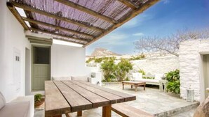 A patio with a wooden table and benches, a thatched roof, and a stone wall.
