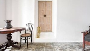 A room with a wooden door, a chair, a table, and a vase.