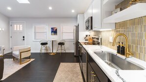 A modern kitchen with a central island, a built-in oven, and a large sink with gold fixtures. - Vibrant Neon Condo Near Restaurants, Coffee & Bars (Nashville)