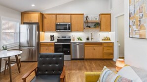 Una cocina moderna con armarios de madera, electrodomésticos de acero inoxidable y un comedor con una silla negra y una mesa de madera.