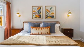 Un dormitorio ordenado con una cama grande, dos mesitas de noche y lámparas fijadas a la pared.