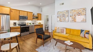 Una cocina moderna con armarios de madera, electrodomésticos de acero inoxidable y un comedor con sofá amarillo y una mesa de centro.