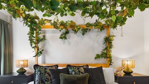 Un dormitorio con un dosel de follaje verde sobre la cama, dos lámparas de noche y una variedad de almohadas.