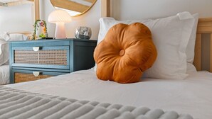 Una cama bien tendida con un edredón blanco y un cojín naranja grande y redondo.