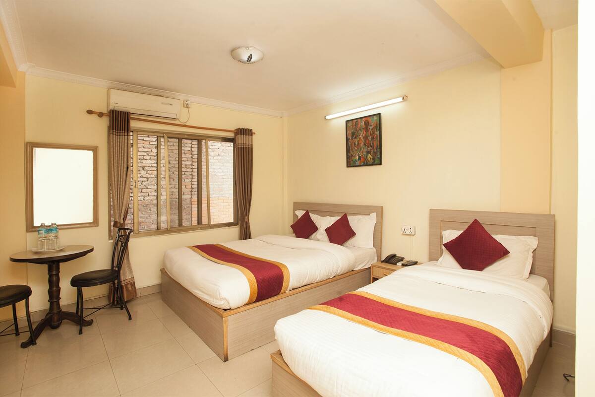A hotel room with two beds, a small table, a chair, and a window with curtains.