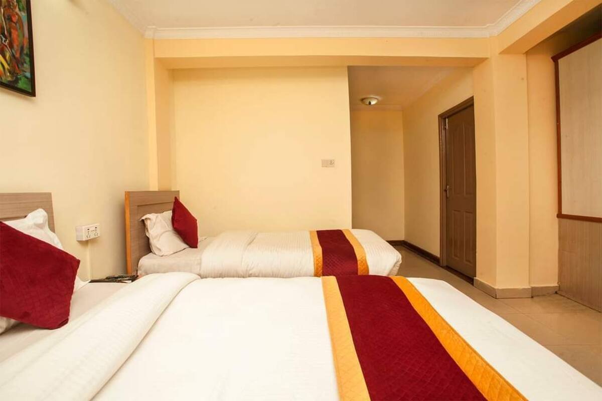 A hotel room with two beds, a wooden headboard, and a door leading to another room.