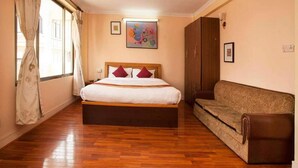 A bedroom with a large bed, a sofa, wooden flooring, and a window with curtains. - Hotel Mountain Gateway (Kathmandu)