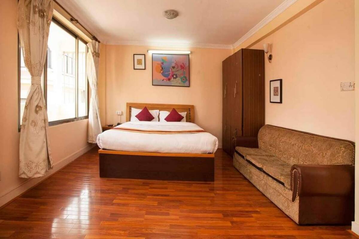 A bedroom with a large bed, a sofa, wooden flooring, and a window with curtains.