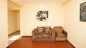 A living room with a patterned sofa and armchair, a wall-mounted artwork, and a door leading to another room. - Hotel Mountain Gateway (Kathmandu)