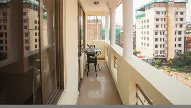 A balcony with a table and chairs, overlooking a residential area with buildings. - Hotel Mountain Gateway (Kathmandu)