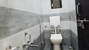 A small, tiled bathroom with a toilet, a shower, and a window. - Shri Nath Hotel And Lodging (Gangapur)