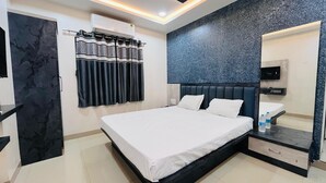 A modern hotel room with a large bed, a bathroom with a mirror, and a wall-mounted air conditioner. - Shri Nath Hotel And Lodging (Gangapur)