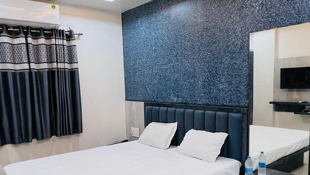 A modern hotel room with a large bed, a bedside table, a built-in TV, and a ceiling fan. - Shri Nath Hotel And Lodging (Gangapur)