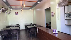 A conference room with tables and chairs, a wooden reception desk, and wall-mounted fans. - Shri Nath Hotel And Lodging (Gangapur)