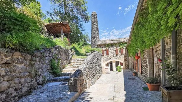 A narrow cobblestone alley with stone walls, a stone staircase, and a building with a tiled roof and arched doorway.