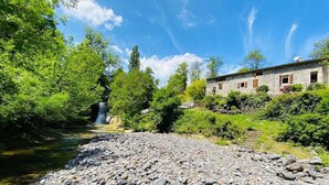 A stone building with a stone roof, surrounded by lush greenery and a small waterfall.