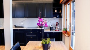 A modern kitchen with dark cabinets, a marble countertop, and a wooden dining table with chairs.