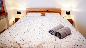 A neatly made bed with floral bedding, two bedside lamps, and a rolled towel on the bed.