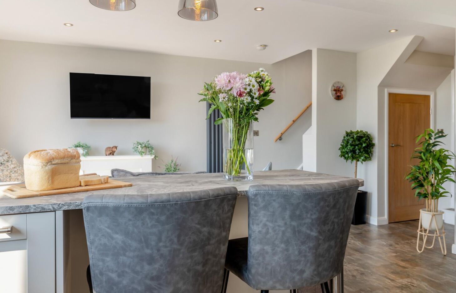 A modern kitchen with a marble countertop, two grey upholstered chairs, a loaf of bread, and a vase with flowers.