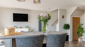 A modern kitchen with a marble countertop, two grey upholstered chairs, a loaf of bread, and a vase with flowers.